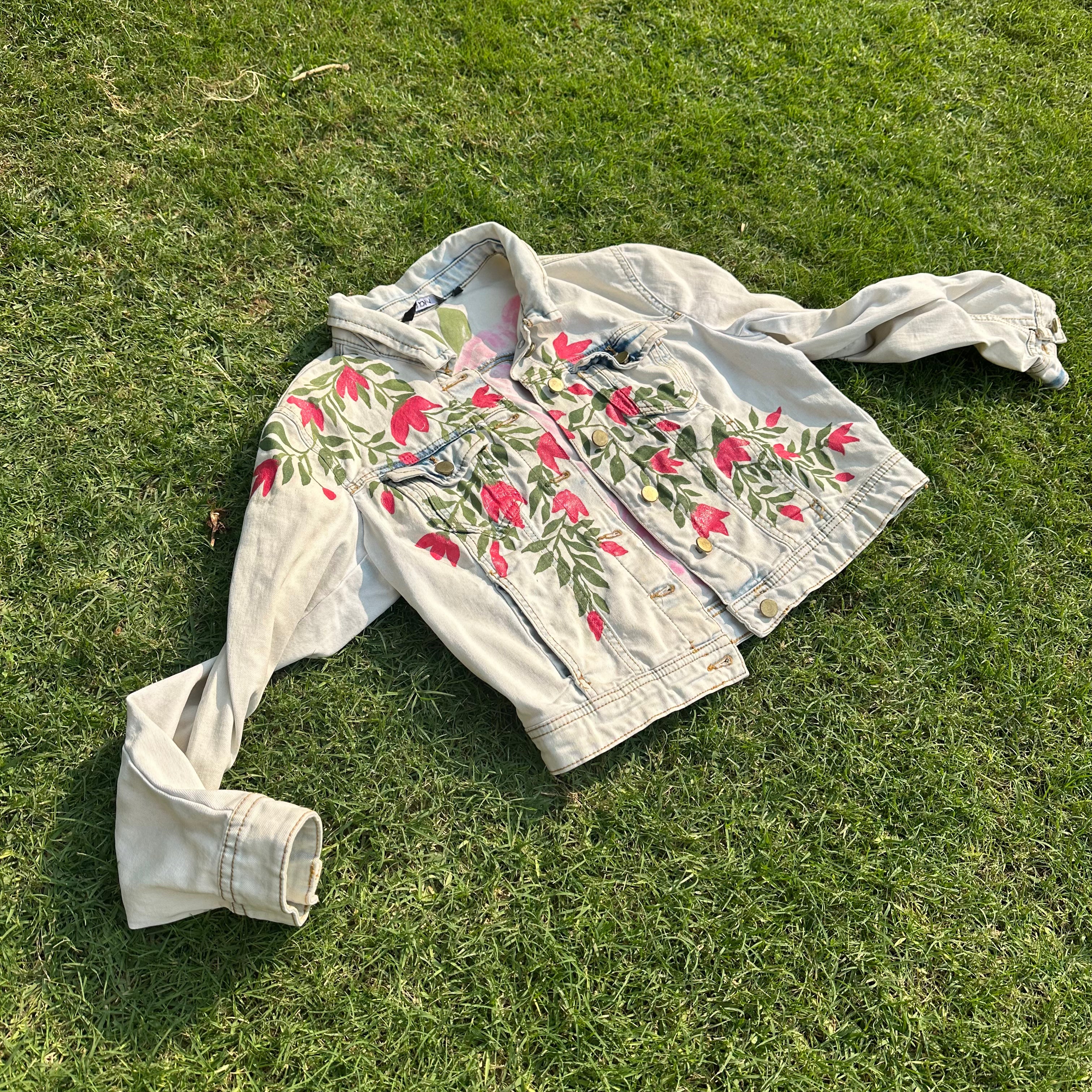Hand-painted floral denim jacket by Handmade Tohfay, cream cropped jean jacket with large pink flower and green vine details.